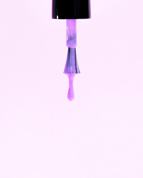 Foto lustrador de unhas violeta brilhante pingando de pincel no pano de fundo rosa