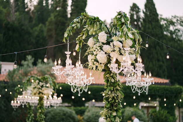 Lustres de cristal e guirlandas decoram o jantar de casamento ao ar livre, entre as árvores