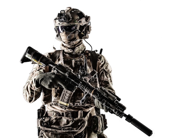 Lutador das forças especiais em uniforme de batalha e capacete com fone de ouvido de rádio, máscara facial e óculos balísticos, em pé com mira a laser equipada e retrato de estúdio de rifle de serviço com silenciador isolado no branco