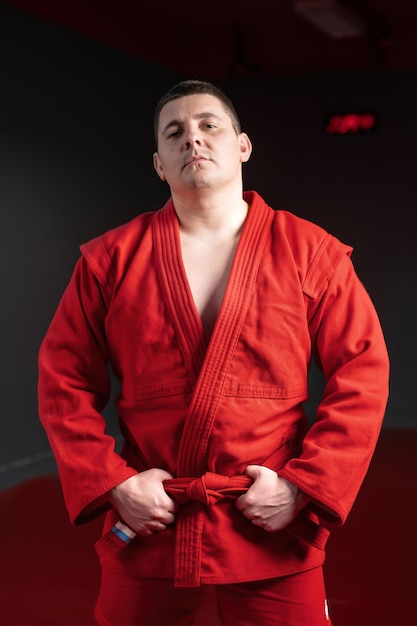 Lutador de artes marciais em quimono vermelho posando e segurando seu cinto