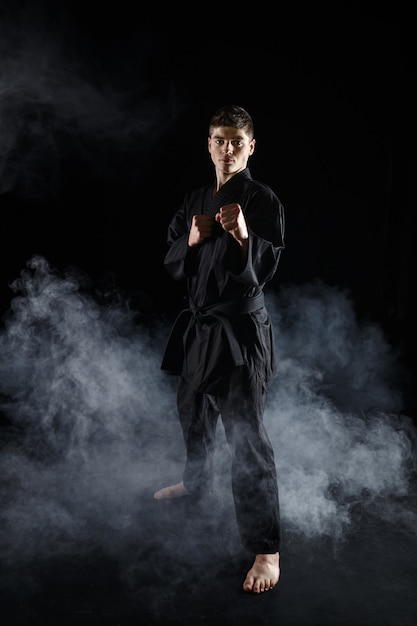 Lutador de caratê masculino no quimono preto, posição de combate. Homem fazendo exercícios, artes marciais, competição de luta