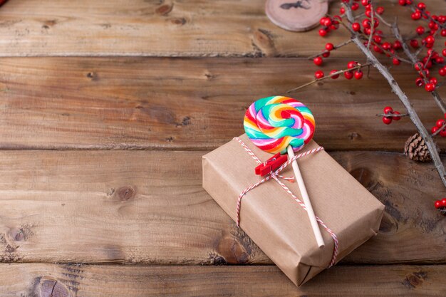 Lutscher mit hellen Streifen und einem Geschenk auf einem hölzernen Hintergrund und einem Zweig mit roten Beeren