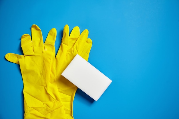Foto luvas amarelas e esponja de melamina branca sobre fundo azul. ferramenta universal para limpar várias superfícies
