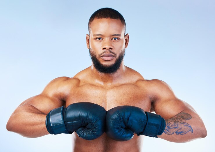Foto luvas de boxe e retrato de um homem negro sério isolado em um fundo azul no estúdio ready fitness e um boxeador africano olhando focado para o desafio de treinamento cardio ou uma luta em um pano de fundo
