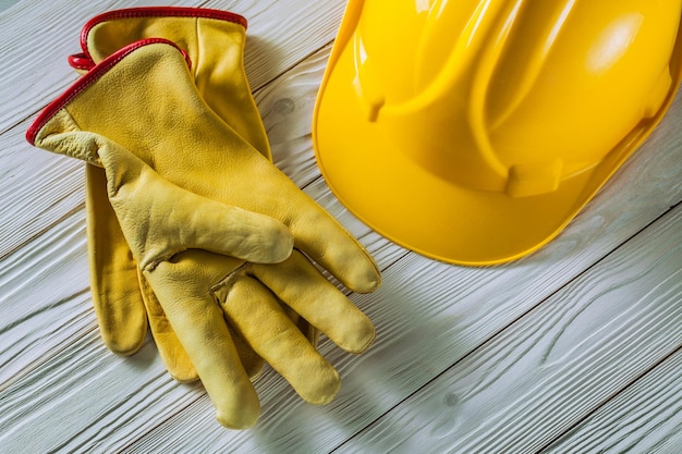 Luvas de trabalho de lether amarelo e capacete de construção em tábuas de madeira pintadas de branco vintage