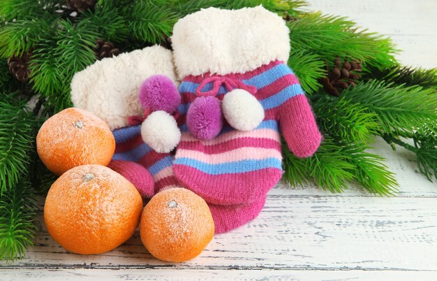 Luvas listradas com galhos de pinheiro e tangerinas em fundo de madeira