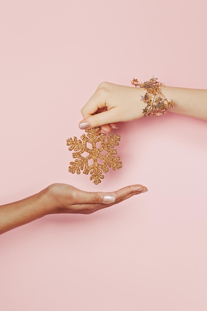 Luxuosa decoração de Natal de ouro floco de neve em mão feminina em fundo rosa com estrelas de confete dourado