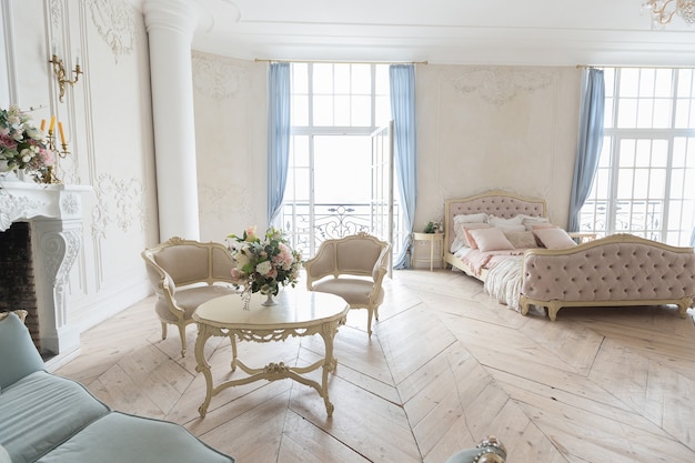 Luxuoso interior claro em estilo barroco. Um quarto espaçoso com uma bela mobília elegante, lareira e flores. estuque de plantas nas paredes e parquet de madeira clara