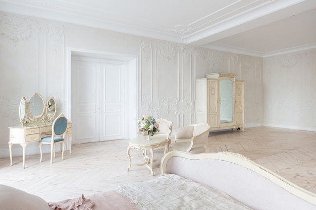 Luxuoso interior claro em estilo barroco. Um quarto espaçoso com uma bela mobília elegante, lareira e flores. estuque de plantas nas paredes e parquet de madeira clara