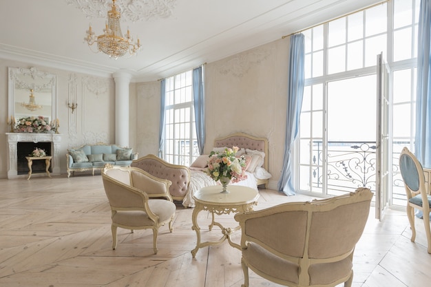 Luxuoso interior claro em estilo barroco. Um quarto espaçoso com uma bela mobília elegante, lareira e flores. estuque de plantas nas paredes e parquet de madeira clara