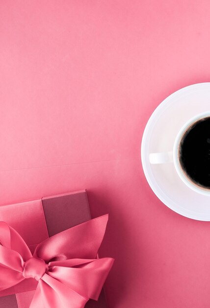 Luxuriöse Geschenkbox und Kaffeetasse auf rosafarbenem Hintergrund, Flatlay-Design für romantische Urlaubsmorgenüberraschung