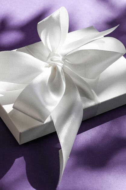 Luxuriöse weiße Geschenkbox für den Urlaub mit Seidenband und Schleife auf violettem Hintergrund Luxuriöses Hochzeits- oder Geburtstagsgeschenk