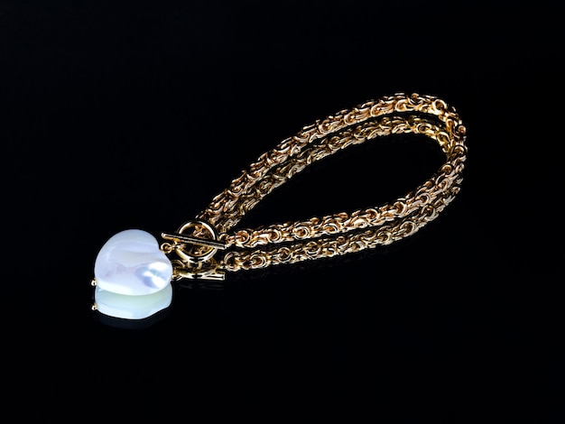 Luxuriöses, elegantes goldenes Armband mit barockem Perlenanhänger auf schwarzem Spiegelhintergrund mit Reflexion Nahaufnahme