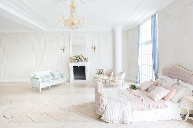 Luxuriöses helles interieur im barockstil. ein geräumiges zimmer mit schicker einrichtung, einem kamin und blumen. pflanzenstuck an den wänden und hellem holzparkett