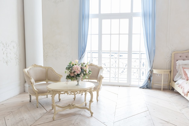 Luxuriöses helles Interieur im Barockstil. Ein geräumiges Zimmer mit schicker Einrichtung, einem Kamin und Blumen. Pflanzenstuck an den Wänden und hellem Holzparkett