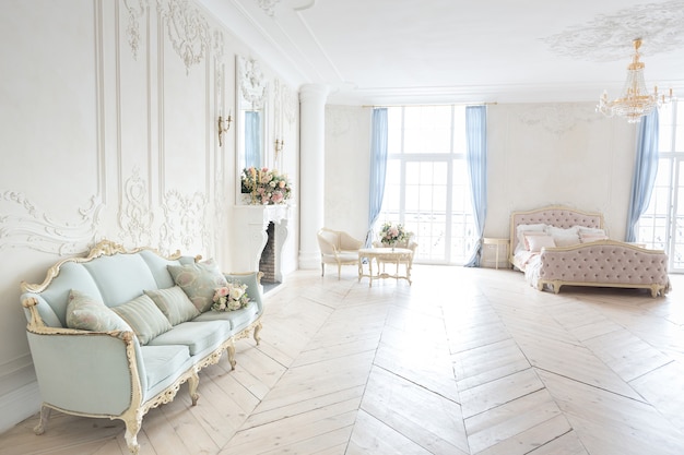 Luxuriöses helles Interieur im Barockstil. Ein geräumiges Zimmer mit schicker Einrichtung, einem Kamin und Blumen. Pflanzenstuck an den Wänden und hellem Holzparkett