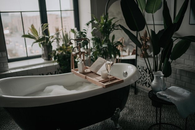 Luxuriöses, modernes Badezimmer im Öko-Stil mit ovaler Badewanne und Champagnerglas bei Tageslicht