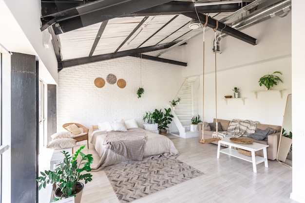 Luxuriöses Schlafzimmerdesign in einem rustikalen Cottage im minimalistischen Stil. weiße Wände, Panoramafenster, Holzdekorationselemente an der Decke, Seilschaukeln mitten in einem geräumigen Raum.