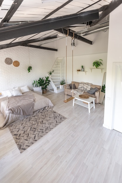 Luxuriöses Schlafzimmerdesign in einem rustikalen Cottage im minimalistischen Stil. weiße Wände, Panoramafenster, Holzdekorationselemente an der Decke, Seilschaukeln mitten in einem geräumigen Raum.