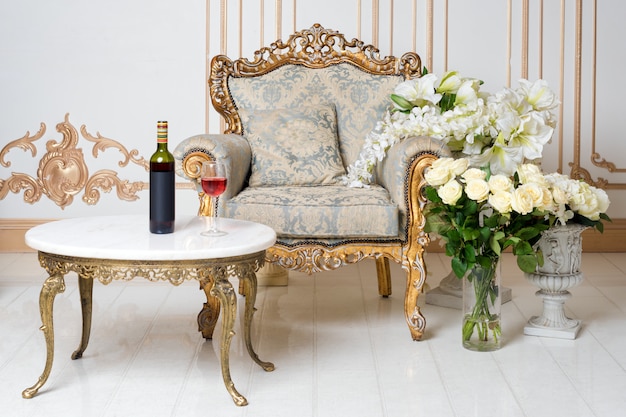Luxuriöses Vintage-Interieur im aristokratischen Stil mit elegantem Sessel und Blumen. Flasche und Glas Wein auf dem Tisch. Retro, Klassiker.