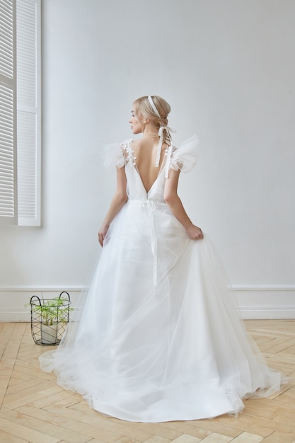 Luxuriöses weißes Hochzeitskleid auf dem Körper des Mädchens. Neue Kollektion von Brautkleidern. Morgenbraut, eine Frau, die vor der Hochzeitszeremonie auf den Bräutigam wartet. Junge Braut in einem langen Kleid