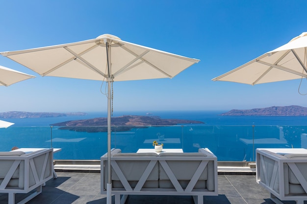 Luxus und Schönheit in Santorini, Griechenland. Terrasse, herrlicher Meerblick, weiße Dekoration, Sonnenschirmstühle