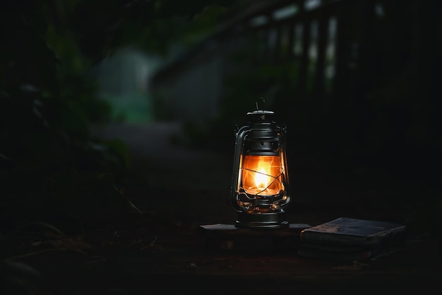 Una luz ardiente, una lámpara roja y un libro iluminan brillantemente un camino forestal nocturno oscuro