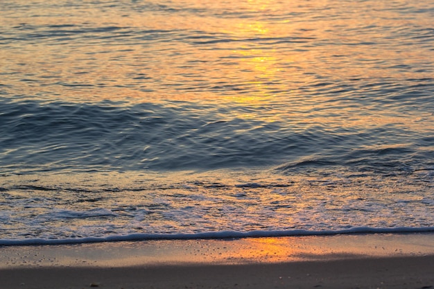 Luz do nascer do sol da manhã brilhando na onda do mar e areia