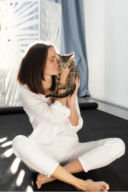 À luz do sol, uma jovem de camisa branca segura um gatinho cinza nos braços