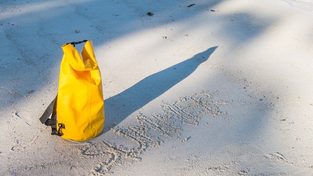 Foto luz e sombra na praia de areia com saco impermeável amarelo e verão manuscrita