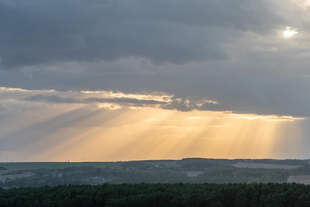 La luz del sol atraviesa las nubes en línea recta y cae sobre la ciudad y el bosque El sol se ocultó detrás de las nubes El bosque en los rayos del sol poniente