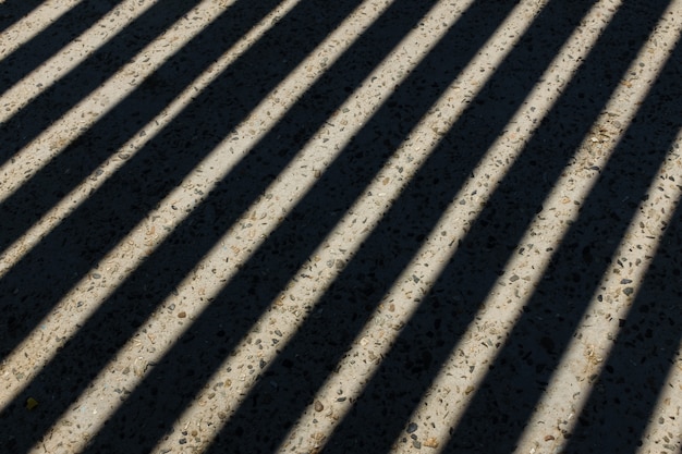 La luz del sol brilla a través de una valla de madera y crea sombras de rayas geométricas en el suelo. Sombras de valla de madera en el suelo. Textura de sombras de valla