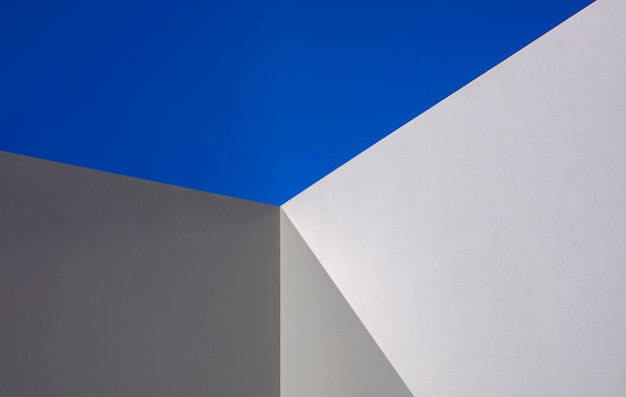 La luz del sol y la sombra en la superficie de la pared de cemento blanco en perspectiva contra el cielo azul claro