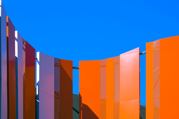 Luz solar e sombra na parede de aço curvada laranja e branca fora do edifício alto contra o céu azul