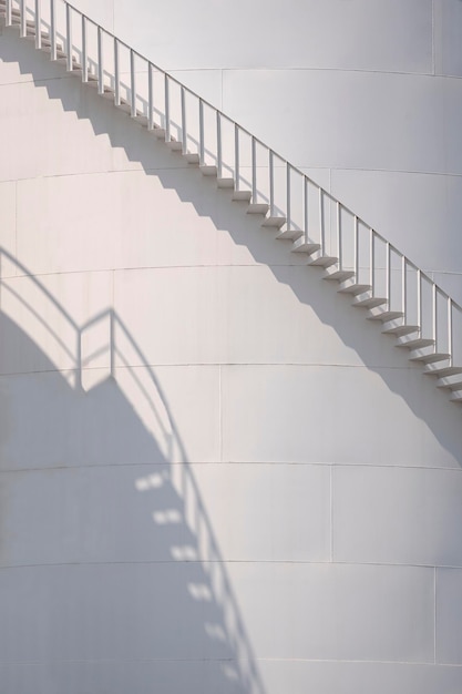 Luz solar y sombra en la superficie curva de la escalera del depósito de combustible de almacenamiento blanco en marco vertical