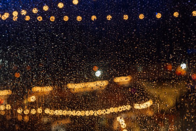 Luzes da cidade à noite durante a chuva atrás de um vidro coberto com gotas de água.