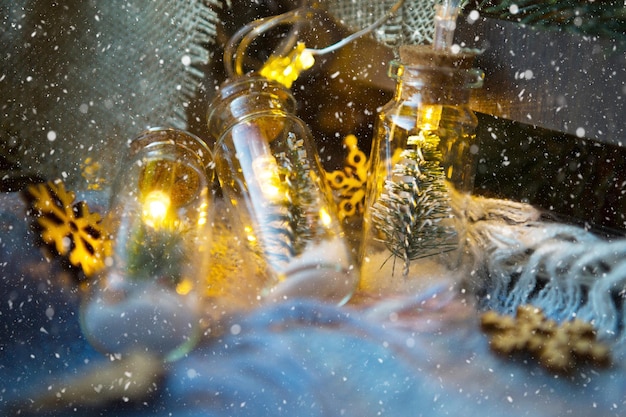 Luzes de fadas em uma jarra com uma árvore de Natal e close-up de neve em uma manta aconchegante e aconchegante com decoração em madeira. Natal e Reveillon, decoração festiva, conforto em casa, preparação para a festa, clima fabuloso