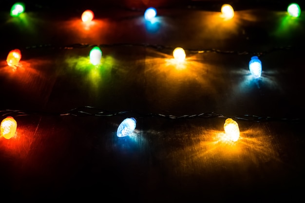 Foto luzes de natal na mesa de madeira. luzes coloridas em uma guirlanda de natal na escuridão da noite