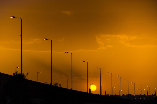 Luzes de rua mostradas em silhueta ao longo da estrada contra o céu dourado do pôr do sol, Riyadh, Arábia Saudita