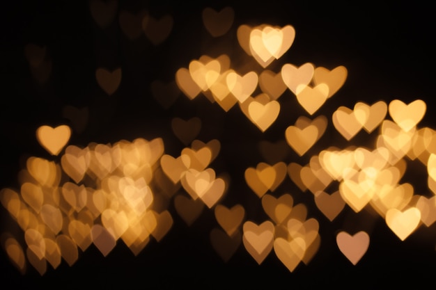 Luzes douradas de desfocagem em forma de coração em fundo preto