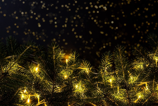 Luzes douradas na árvore de Natal no fundo desfocado com brilhos no escuro