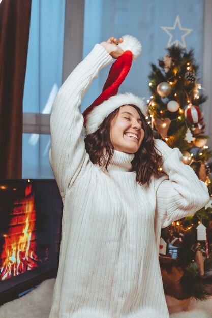 Lviv, Ucrania - 15 de diciembre de 2021: joven mujer bonita sentada cerca del árbol de Navidad bebiendo una taza de café copia espacio