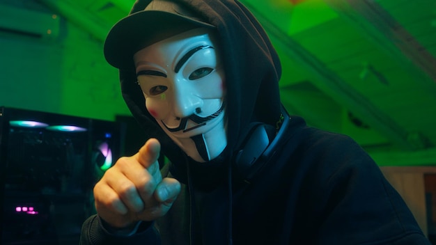 Lviv, Ucrania 3 de junio de 2024 Hacker anónimo escribiendo computadora mirando a la cámara apuntando con el dedo programador ataque ciberespacio fraude ladrón spyware internet virus pc estafa red código binario cortafuegos