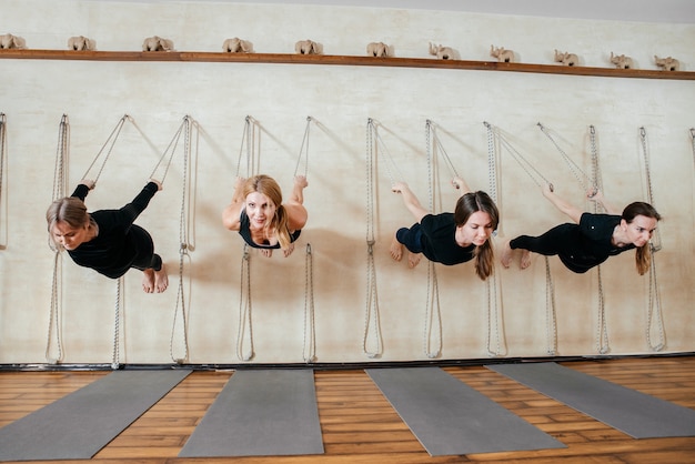 Lyengar grupo femenino de yogui practicando ejercicios de calistenia en el estudio de yoga colgado en una pared con