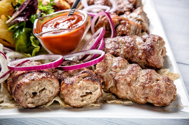 Lyulya kebab con salsa roja y cebolla en plato blanco de cerca