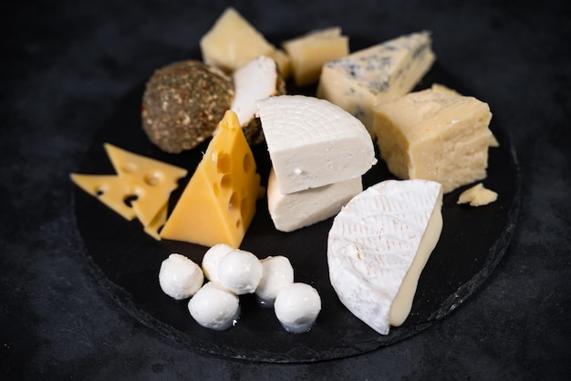 Maasdam, mozzarella, camembert y otros tipos de deliciosos quesos amarillos y blancos sobre un fondo oscuro. Un manjar de lujo caro.