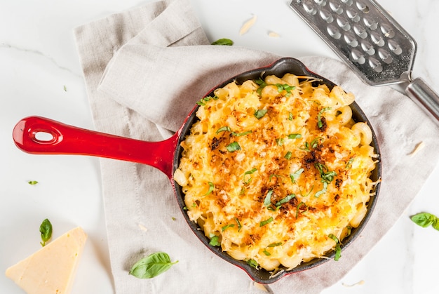 Mac und Käse, amerikanische Makkaroniteigwaren mit käsiger Soße und knuspriger Brotkrumenbelag, in portionierter Wanne, weiße Marmortabelle, Draufsicht copyspace