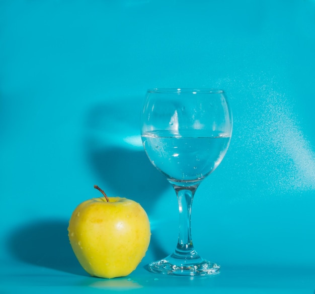 Maçã amarela com um copo de água sobre um fundo azul.