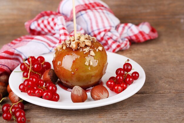 Maçã doce de caramelo no palito com bagas, na mesa de madeira