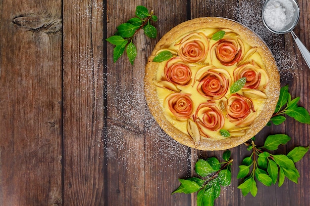 Maçã em forma de rosas na torta na mesa de madeira rústica.